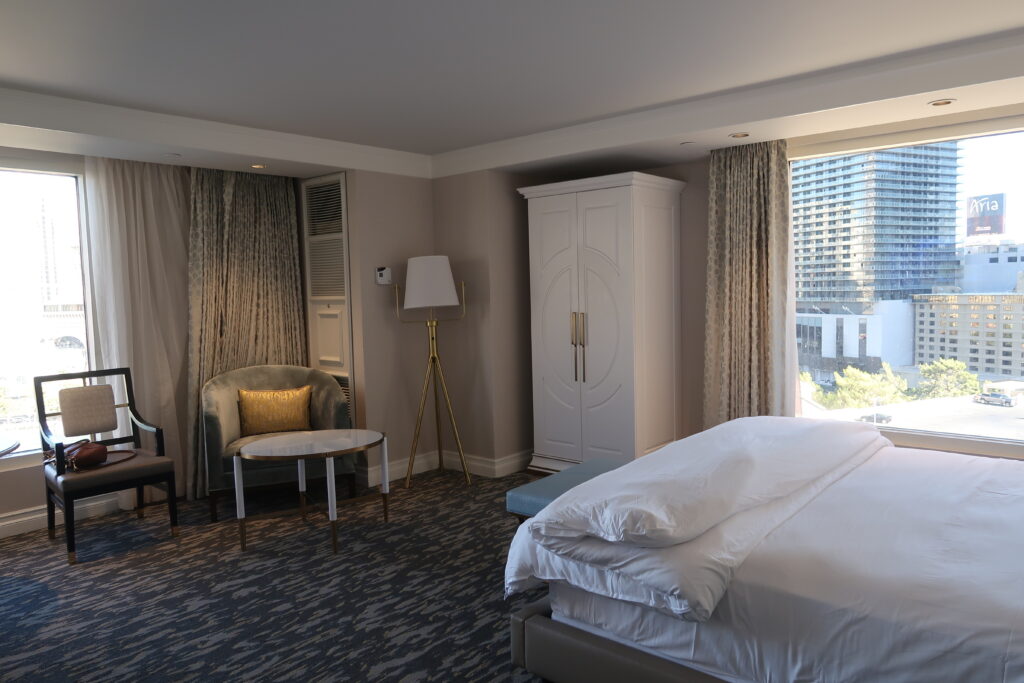 Bellagio room with bed with white linens on the right, two windows besetting the corner and a lounge chair.