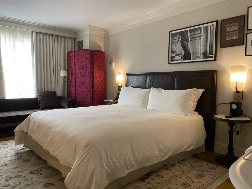 Bed with white linens on area rug with brown leather headboard.