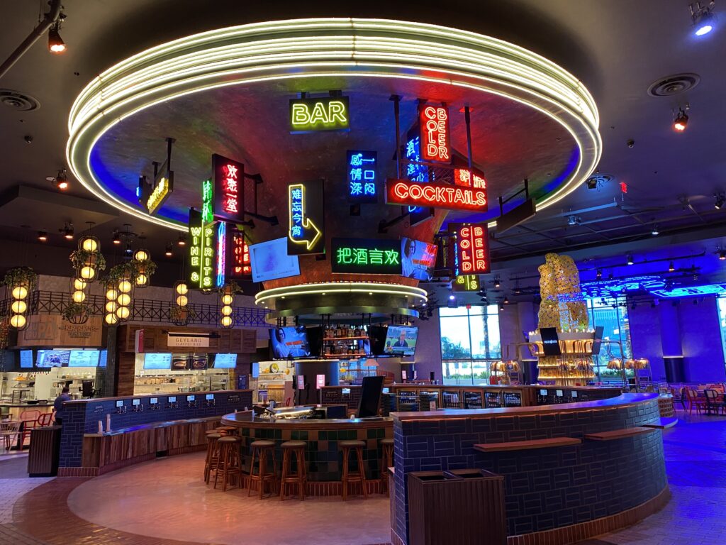Center of a food court with neon signs.