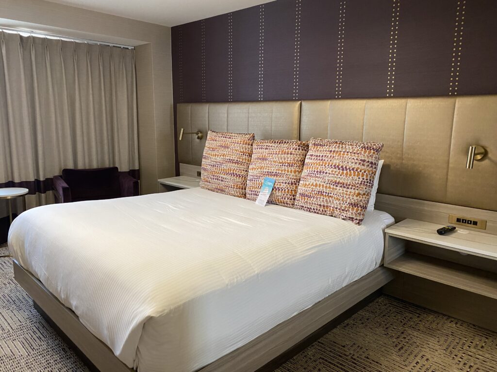 Bed with white linens, gold headboard and purple wall.