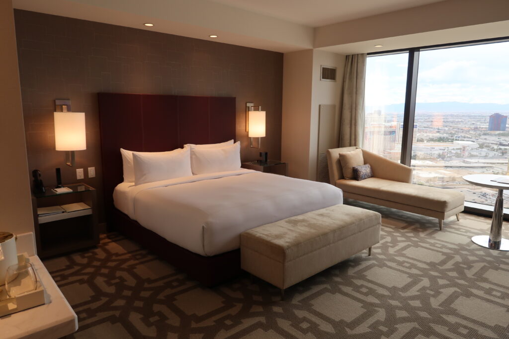 Bed with purple headstand and white linens on a gray carpet.