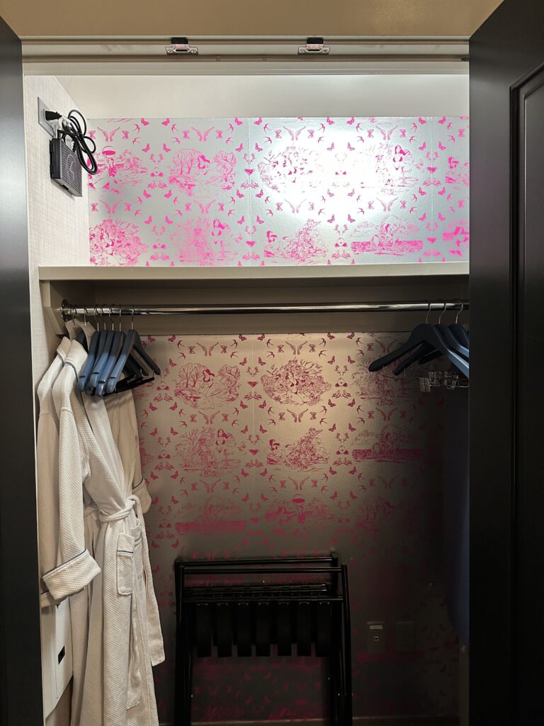 Clost with pink wallpaper and a white robe. 